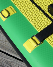 Close-up of a green and yellow inflatable stand-up paddle board with black straps and buckles, resting on a weathered wooden dock.