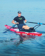 A man wearing a black T-shirt and shorts rows a red and white paddle board with black oars on deep blue calm water.