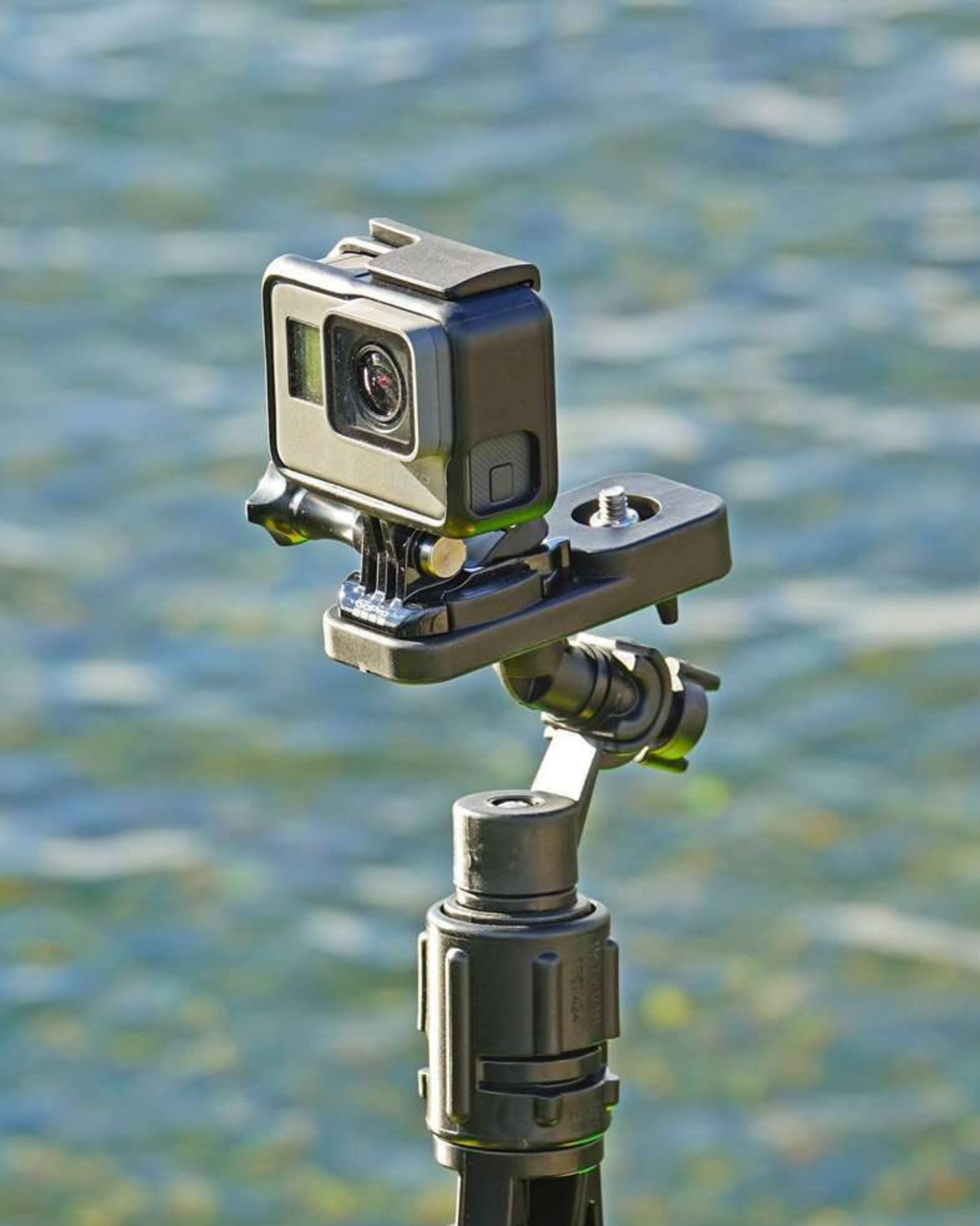 A black adjustable mount bracket holding an action camera with a blurry ocean background.