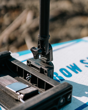 Close-up of rigging component mounted on a white and blue paddle board outdoors, with blurred natural background.