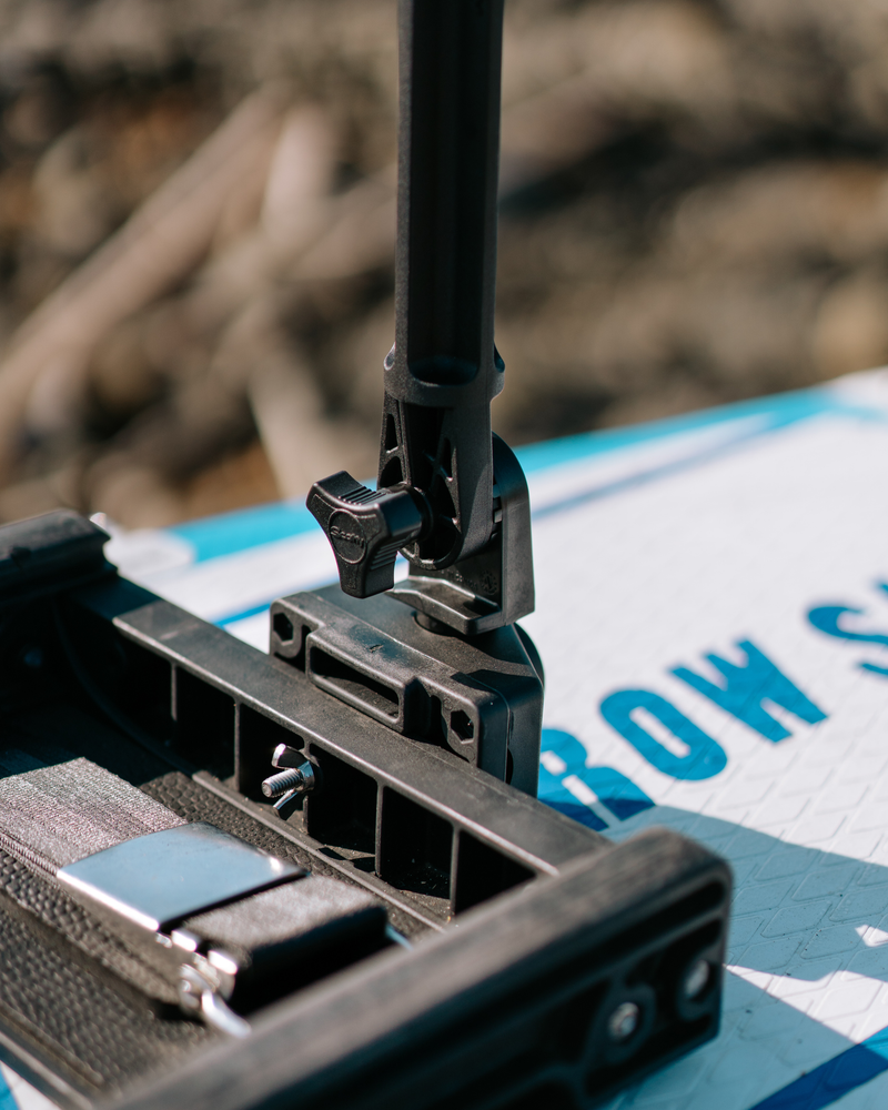 Close-up of rigging component mounted on a white and blue paddle board outdoors, with blurred natural background.
