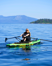 A woman rows on a green and black stand-up paddleboard on calm blue water.