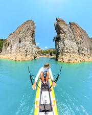 A person rowing a yellow paddleboard in bright turquoise water between two large rocky cliffs under a clear blue sky.