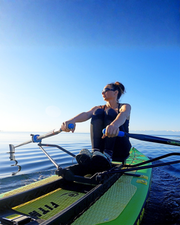 A woman wearing sunglasses rows a green and yellow stand-up paddleboard on open water, holding a oars under a clear blue sky.