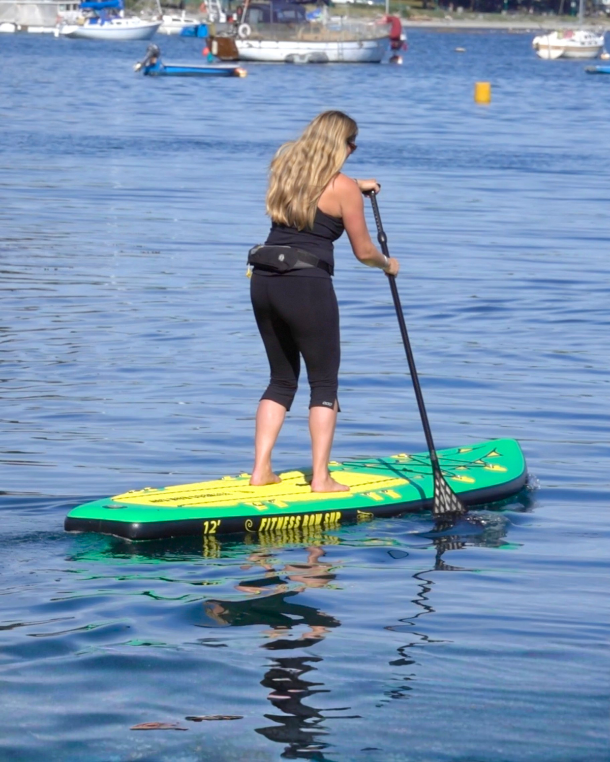 Woman Stand Up Paddle Boarding on a green and yellow paddle board holding a black carbon fibre paddle.