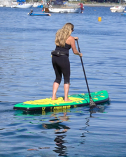 Woman Stand Up Paddle Boarding on a green and yellow paddle board holding a black carbon fibre paddle.