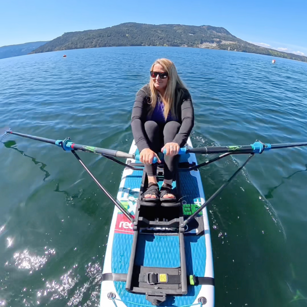 A woman dressed all in black rows a white and blue paddle board holding oar handles in both hands. 