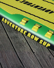 Close-up of an inflatable paddle board on dark wooden planks, showing a yellow and green deck with black and yellow 'ADVENTURE ROW SUP' branding and three yellow handle straps.