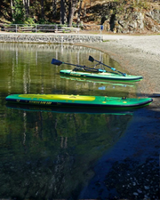 Two green and yellow paddle boards floating in the shallows, one with a rowing system on and one without. A sandy beach is visible. 