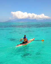 A man rowing the oar board rowing kit on an inflatable paddle board on bright turquoise ocean water.